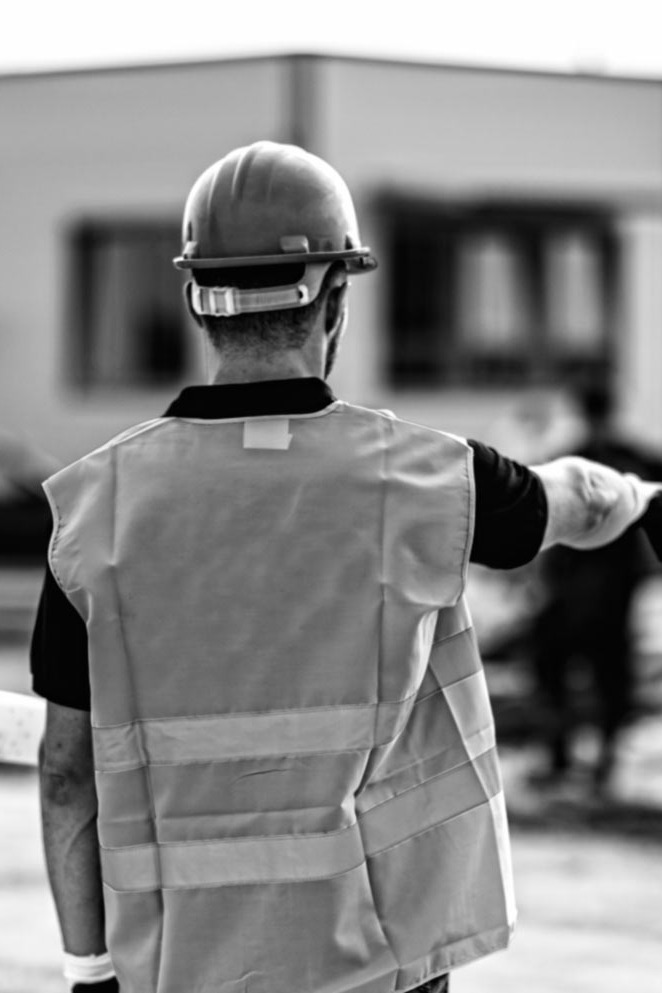 Deux contremaîtres en casque et dossard discutent sur un chantier, une bétonnière derrière eux, photo en noir et blanc