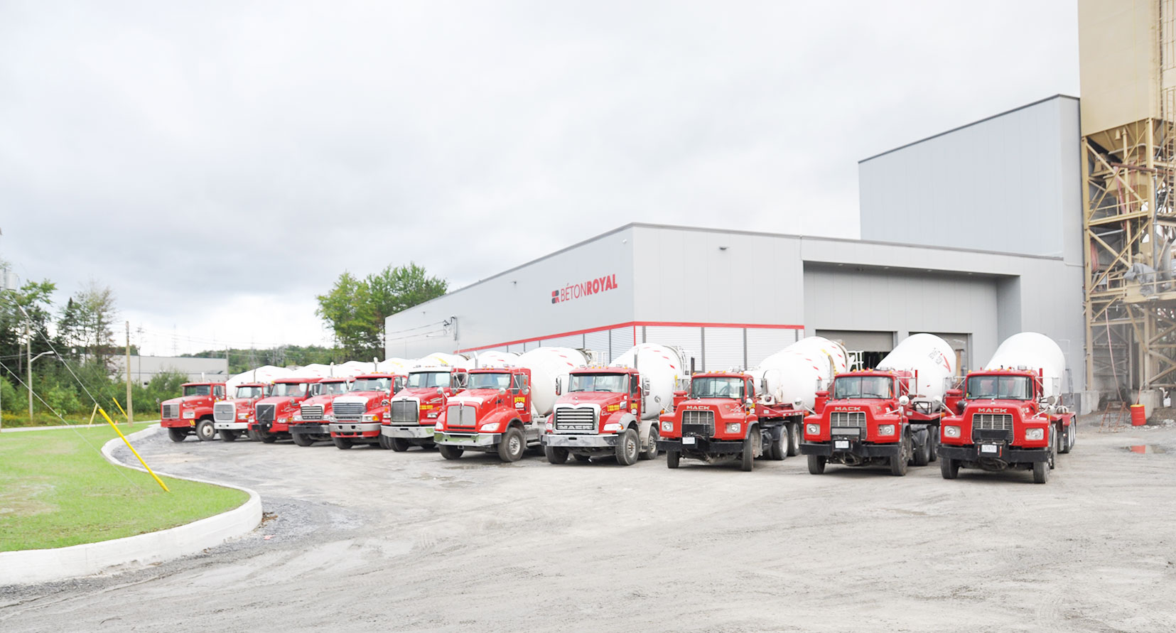 Une dizaine de bétonnières rouges alignées devant l'usine Béton Royal, le silo derrière
