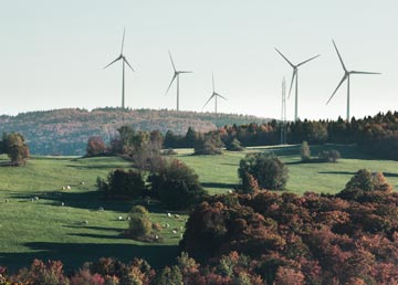 Des éoliennes alignées sur la crête, au-dessus des champs et des boisés d'automne