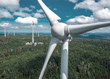 Une éolienne vue de haut, ses trois pales au-dessus de la forêt et du parc éolien